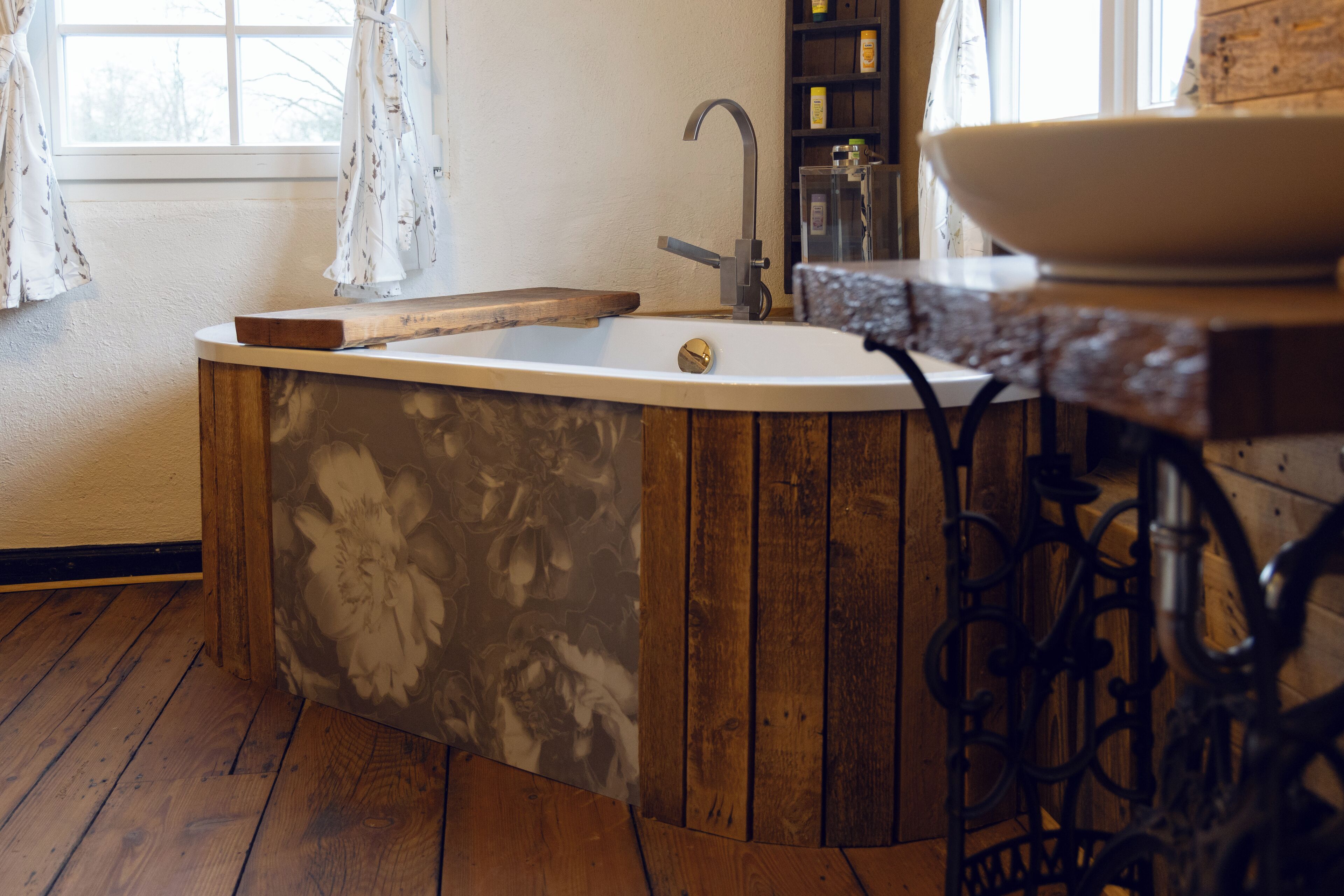A bathroom with a wooden bathtub, a white sink, and a wooden shelf with toiletries.