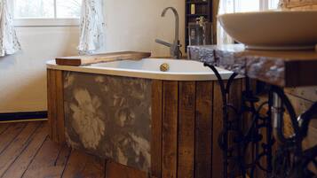 A bathroom with a wooden bathtub, a white sink, and a wooden shelf with toiletries.