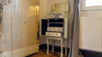 A room with a wooden floor, a white radiator, a grey curtain, and a small white table with drawers.