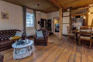 Un salon chaleureux avec un canapé en cuir marron, une table à manger en bois et des chaises, ainsi qu’une cheminée.