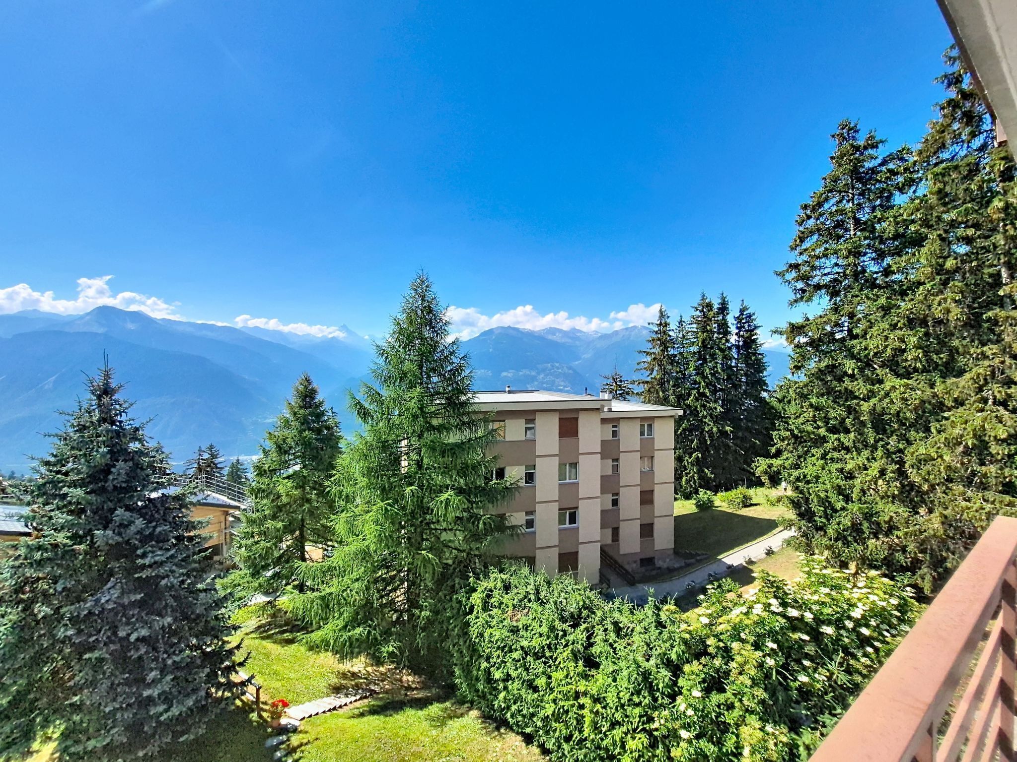 A multi-story building surrounded by dense greenery and mountains in the background.