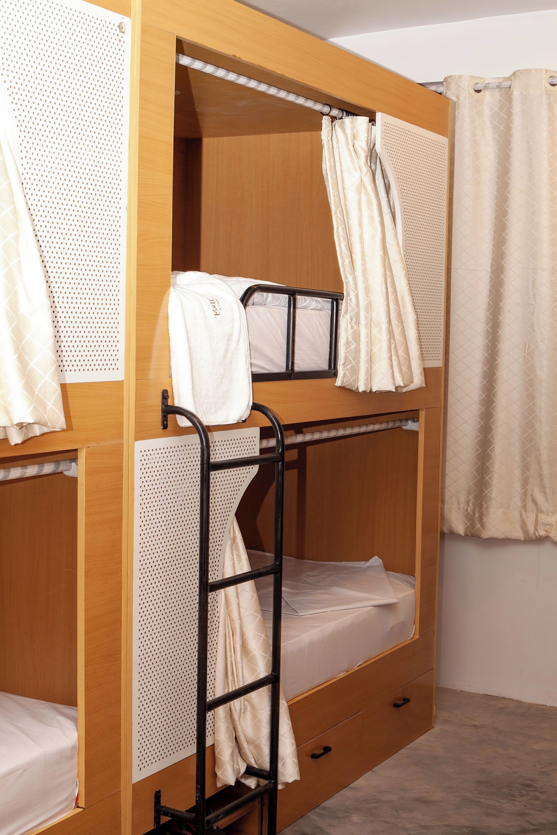 Une chambre avec un lit superposé, une structure en bois, une échelle en métal et un petit tiroir.