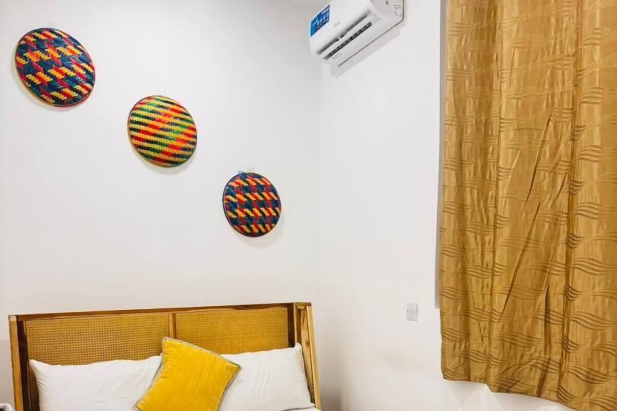 A room with a bed, a wall-mounted air conditioner, and three decorative wall hangings.