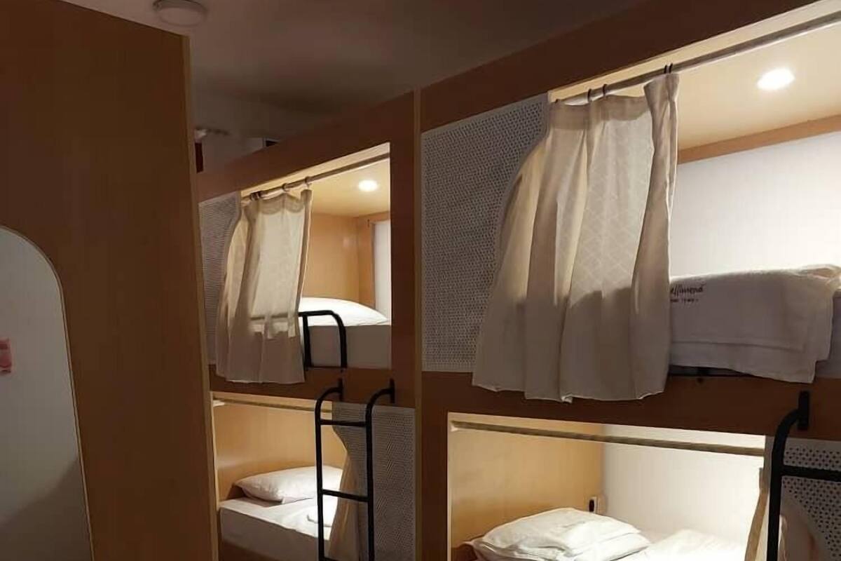 A dormitory room with bunk beds, a small window, and a woven mat on the floor.