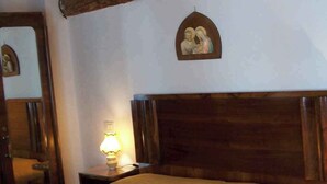 A bedroom with a wooden headboard, a bed with a beige bedspread, a nightstand with a lamp, and a wall-mounted religious icon. - Cozy house in the heart of the Euganean Hills, a stone's throw from the center of Este. (Este)