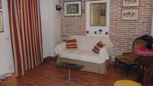 A living room with a sofa, a small table, a chair, and a patterned curtain. - Cozy house in the heart of the Euganean Hills, a stone's throw from the center of Este. (Este)