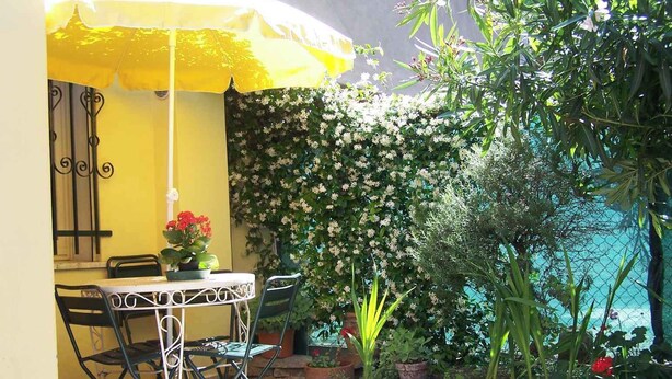 A patio with a yellow umbrella, a table, and chairs. There is a wall with climbing plants and a view of a body of water. - Cozy house in the heart of the Euganean Hills, a stone's throw from the center of Este. (Este)