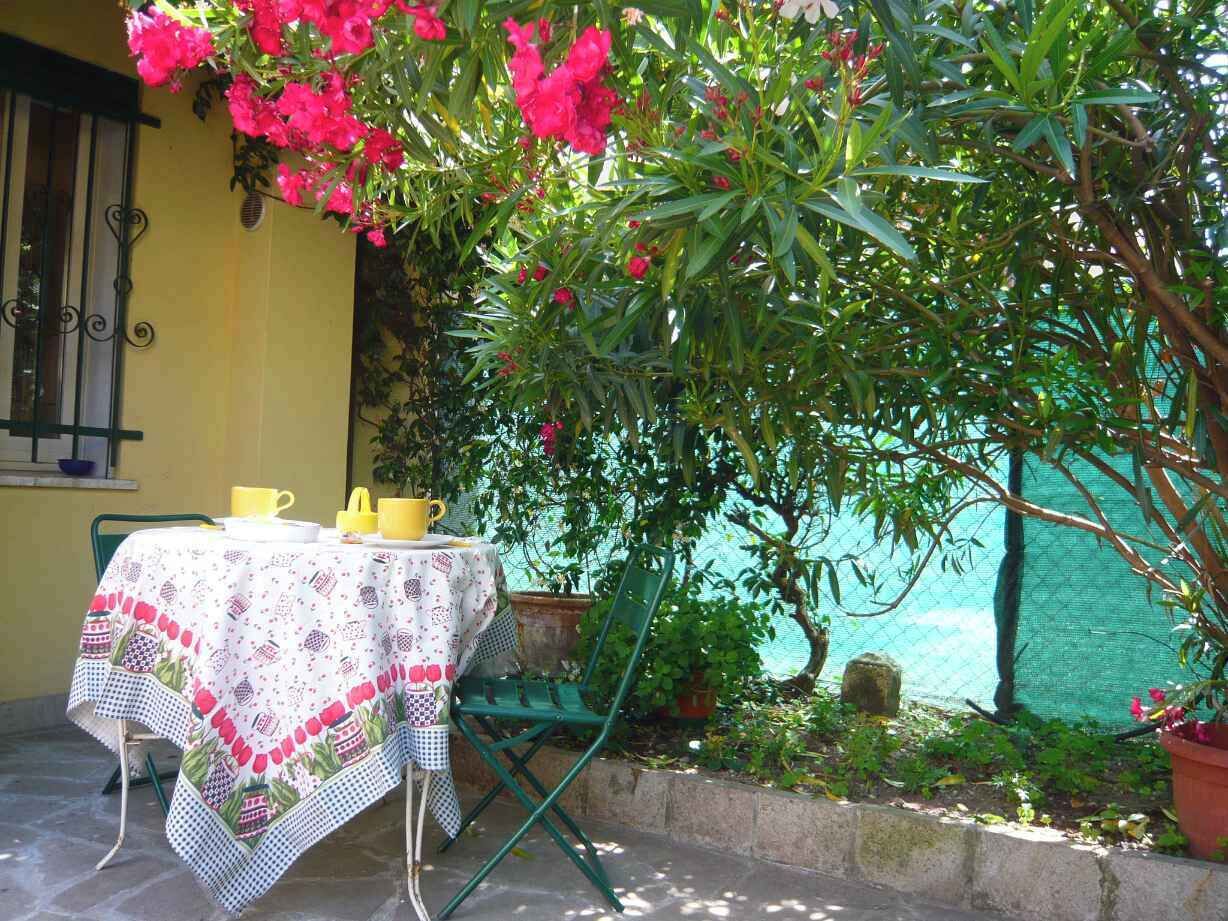 Un área de comedor al aire libre con una mesa dispuesta para dos personas, rodeada de exuberante follaje y flores vibrantes.