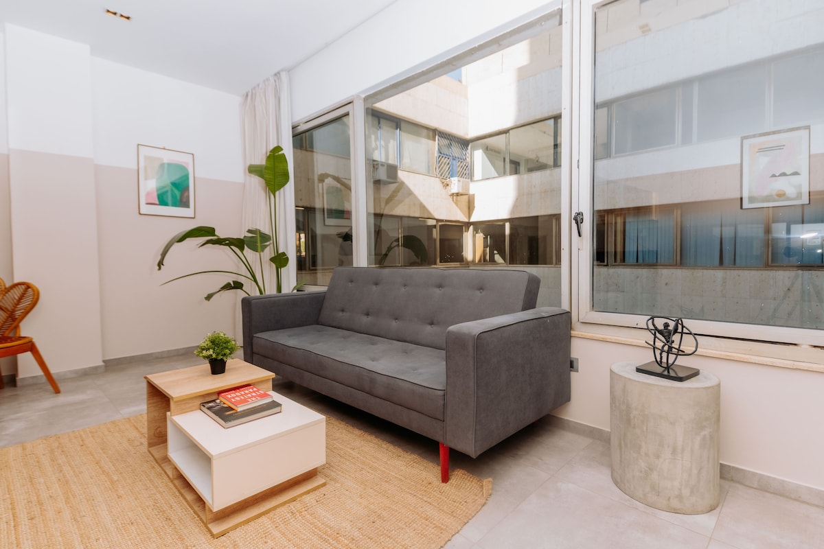 A modern living room with a grey sofa, a wooden coffee table, a small plant, and a concrete side table.