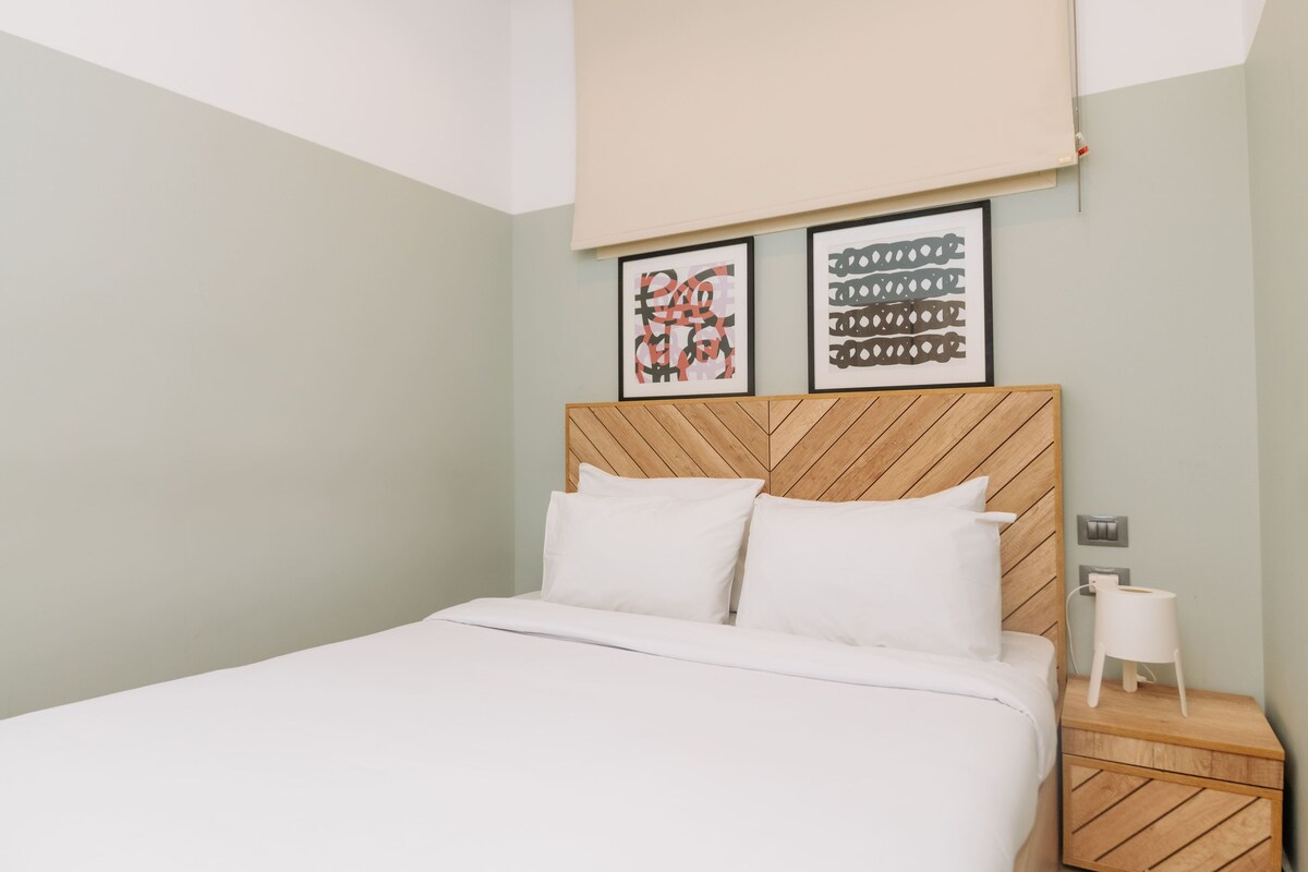 A neatly made bed with white bedding, a wooden headboard, and two framed artworks on the wall.