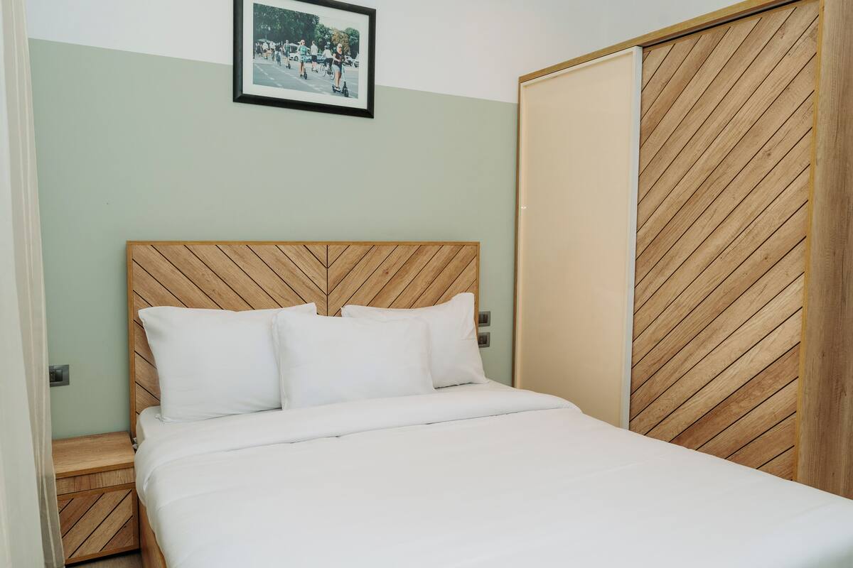 Una cama bien hecha con tablero de madera, una mesita de noche y un armario con patrón de espiga.