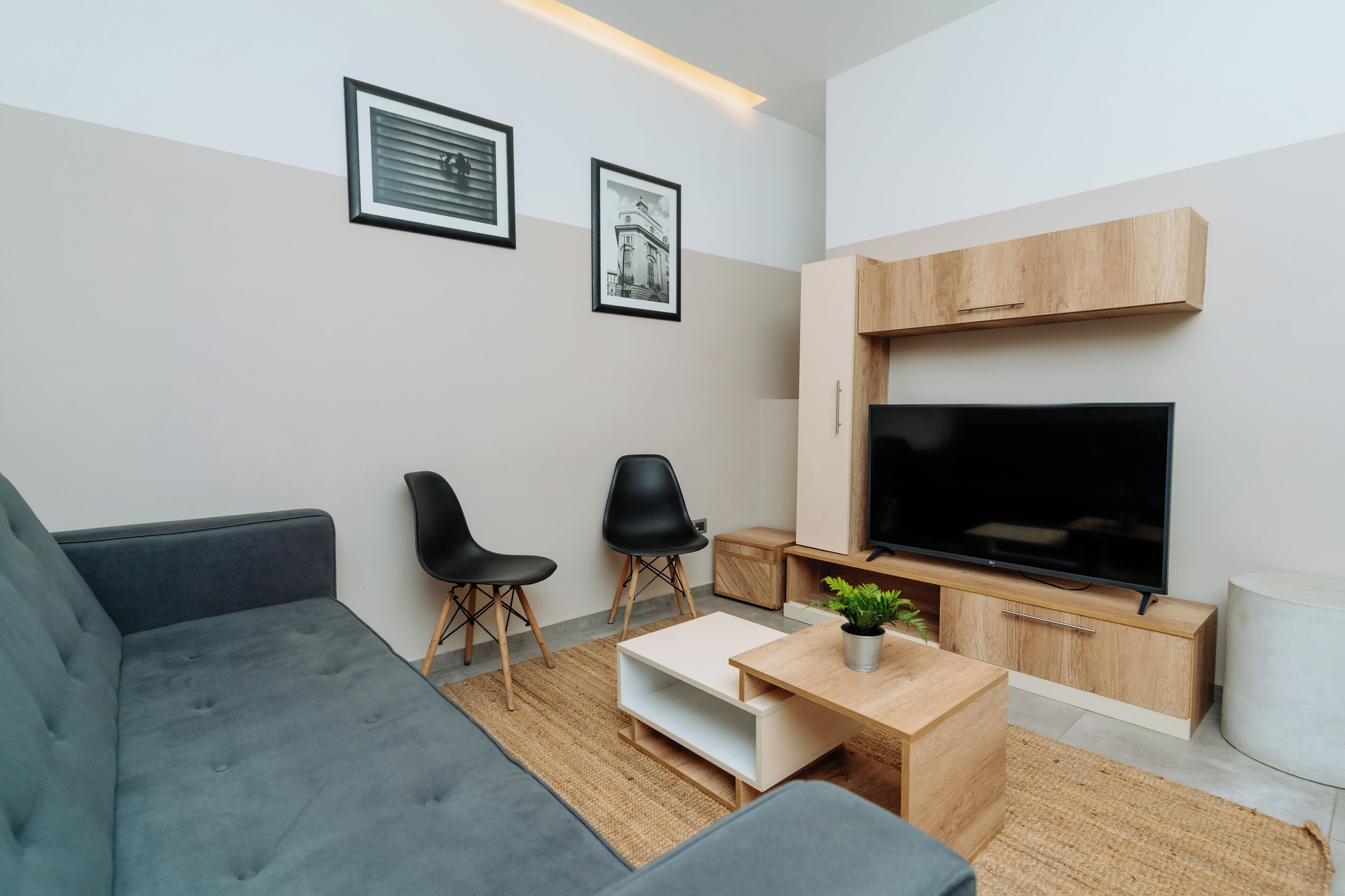Una sala de estar moderna con un sofá gris, dos sillas negras, una mesa de centro de madera, un televisor de pantalla plana y un mueble de pared.
