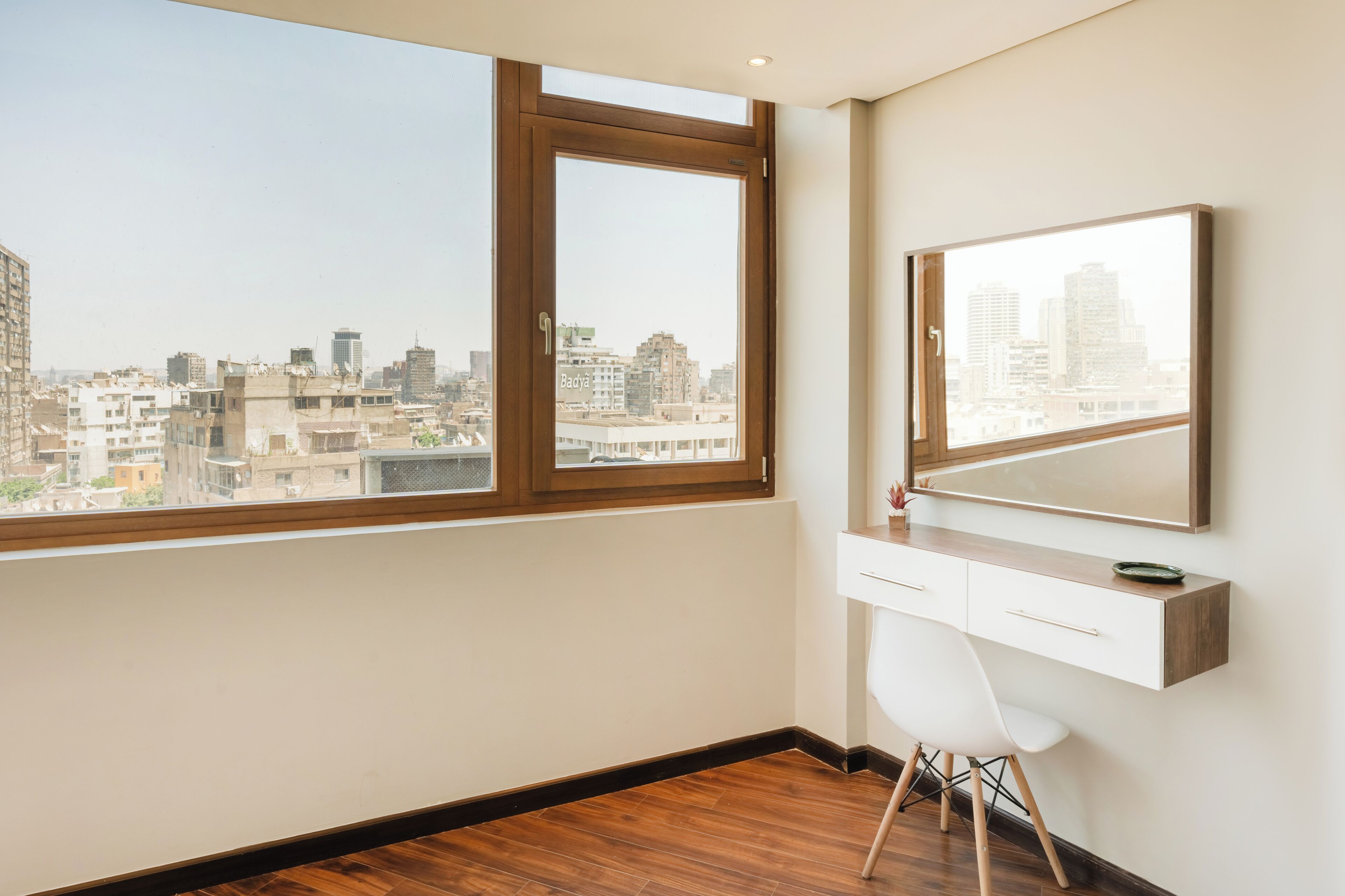 A room with a large window, a desk with a chair, and a mirror on the wall.
