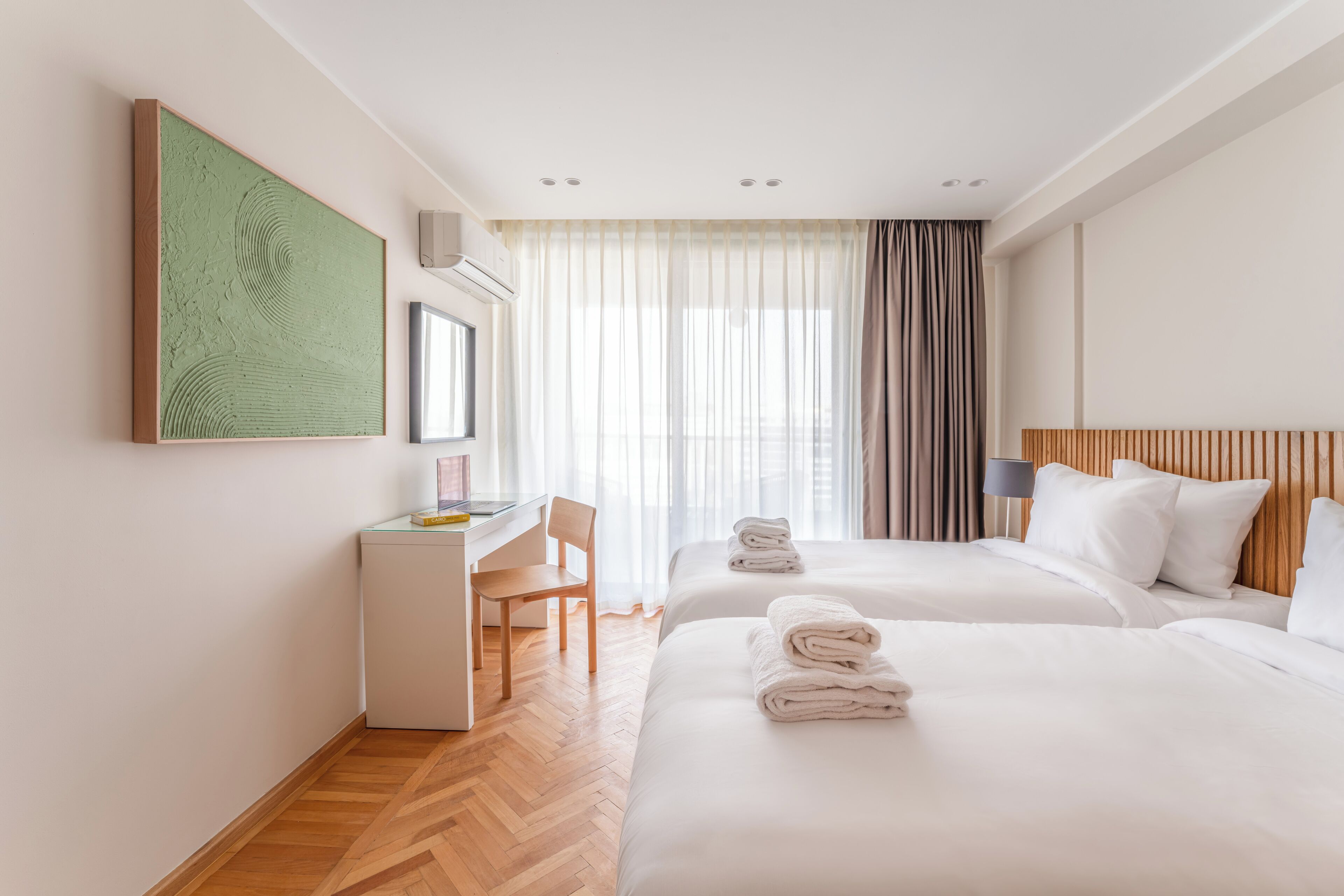 Een hotelkamer met twee bedden, een bureau, een stoel en een groot raam met gordijnen.