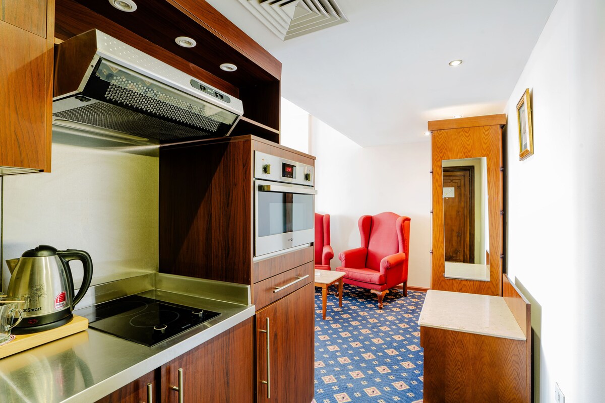 Una kitchenette compacta con estufa, microondas y una silla roja en la esquina.