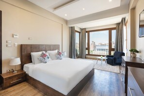 Een hotelkamer met een groot bed, een bureau, een stoel en uitzicht op de stad.