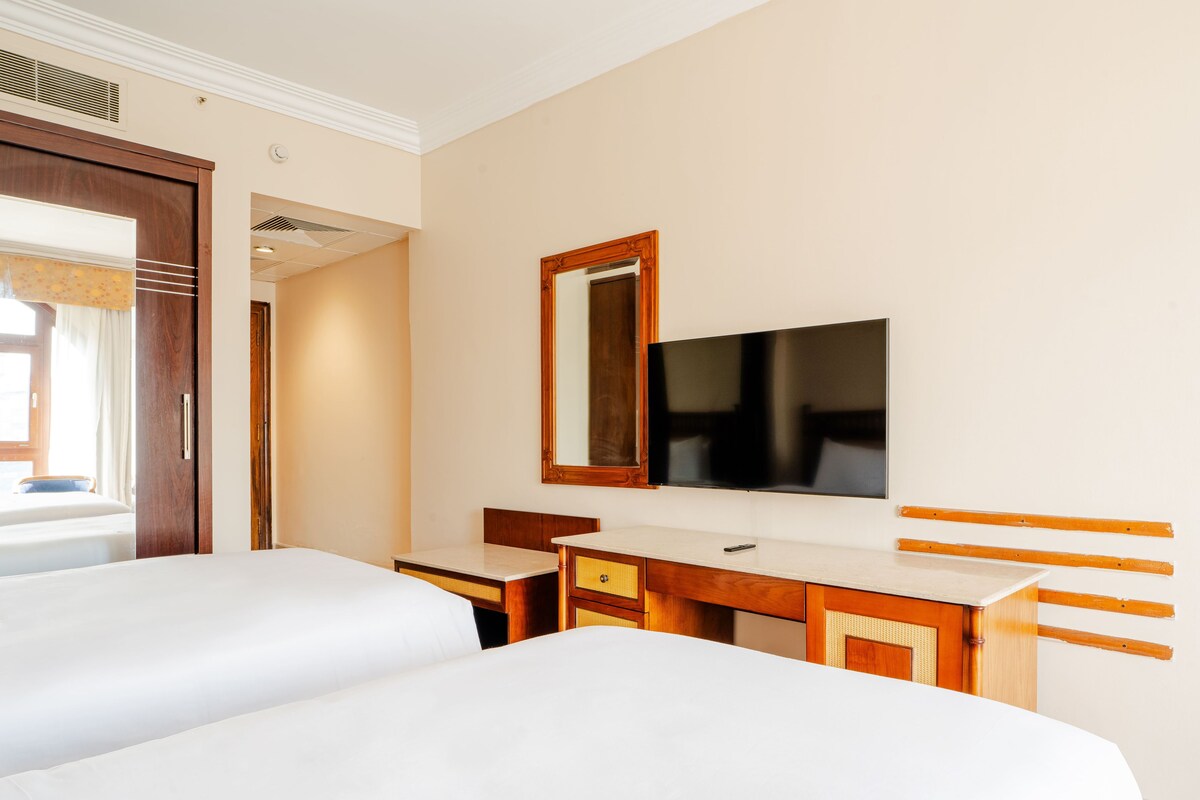 Une chambre d’hôtel avec deux lits, un bureau, un miroir et une télévision.