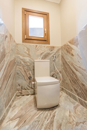 Een badkamer met toilet, marmeren wanden en een raam boven het toilet.