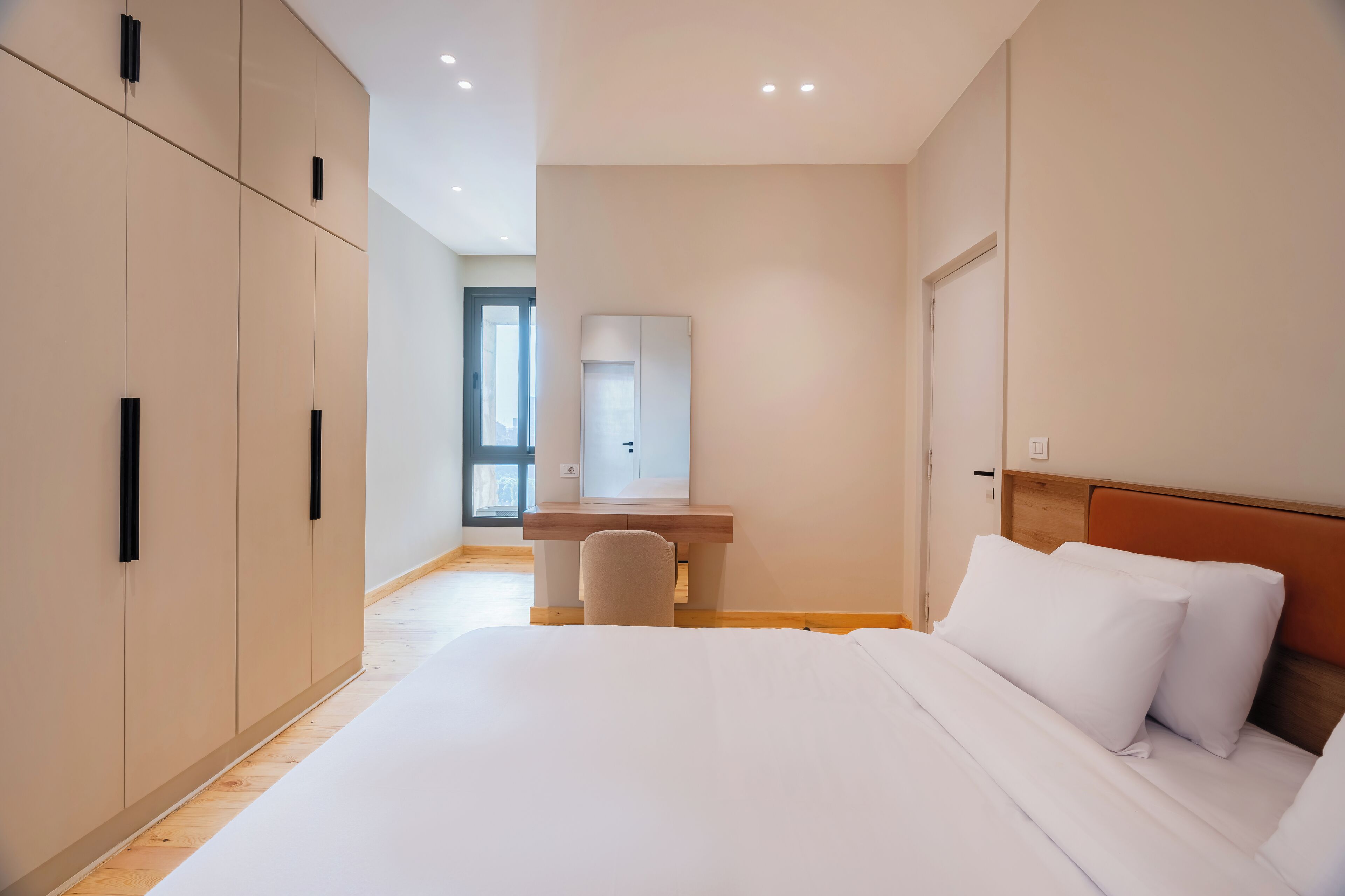 A modern hotel room with a large bed, a desk, and a wardrobe.
