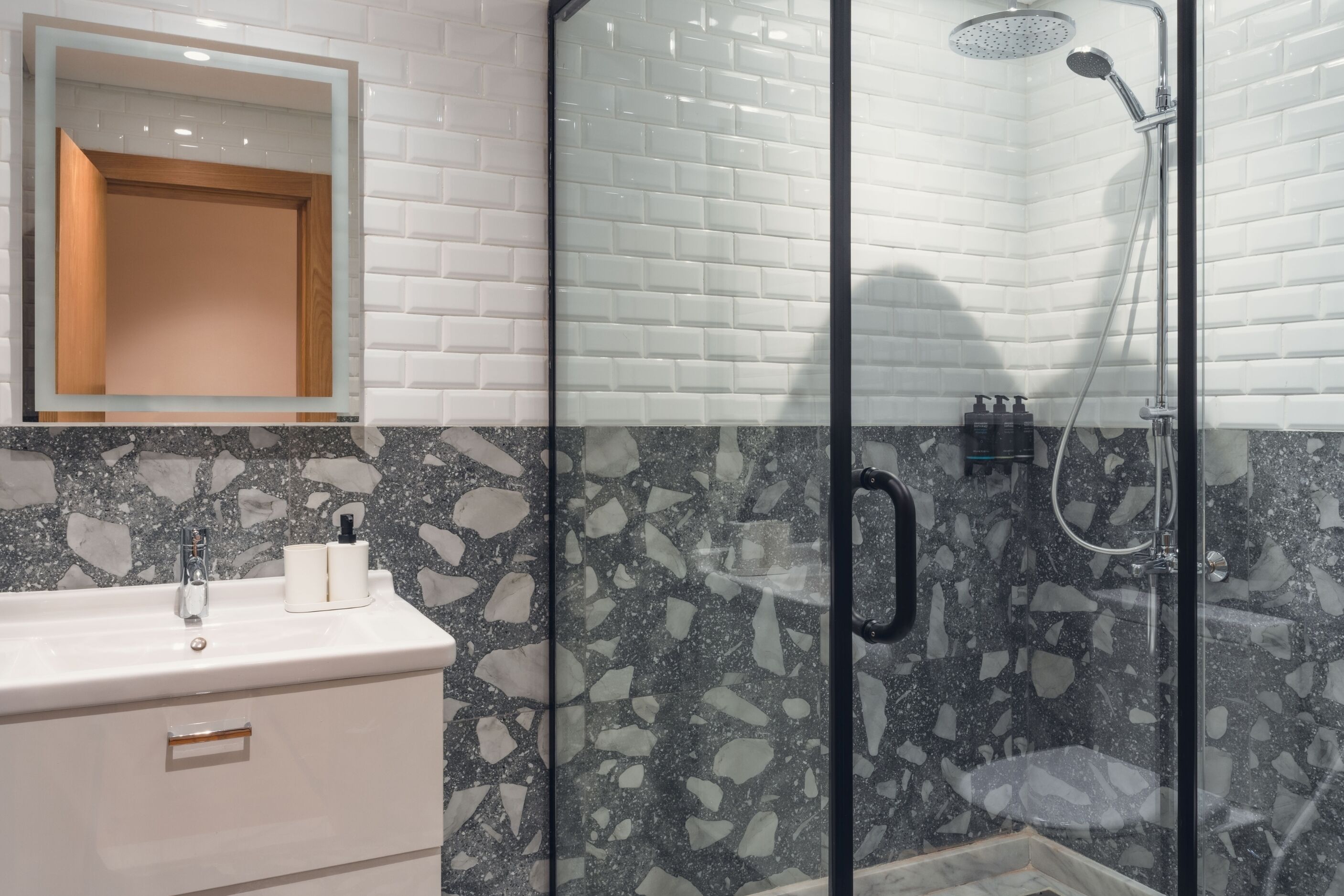 Ein Badezimmer mit weißem Waschbecken, einem Spiegel, einer Dusche mit Glastür und einem Terrazzo-Boden.