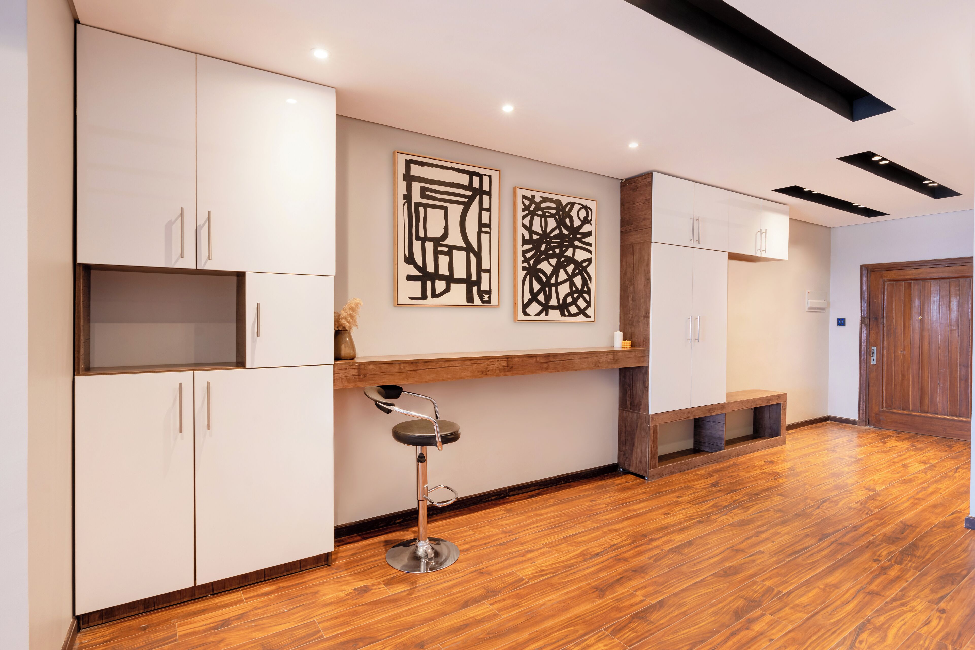 A modern kitchen with white cabinets, a wooden bench, and two abstract art pieces on the wall.