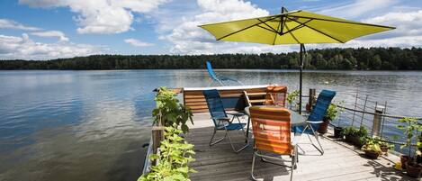 Eine Holzterrasse mit Tisch, Stühlen und Sonnenschirm mit Blick auf einen stillen See.