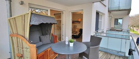 A balcony with wicker furniture, a round table, and a potted plant.