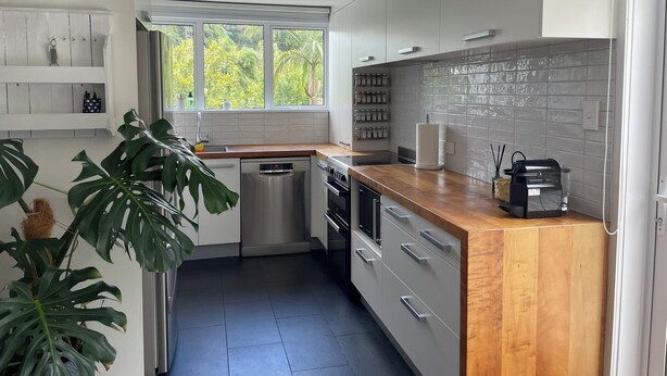 Una cucina moderna con mobili bianchi, un piano di lavoro in legno, una lavastoviglie e una finestra con vista sul verde.