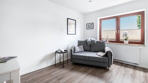 A modern living room with a grey sofa, a small side table, a white radiator, and a window with blinds. - Apartment '2' with Wi-Fi (Weddingstedt/OT Weddinghusen)