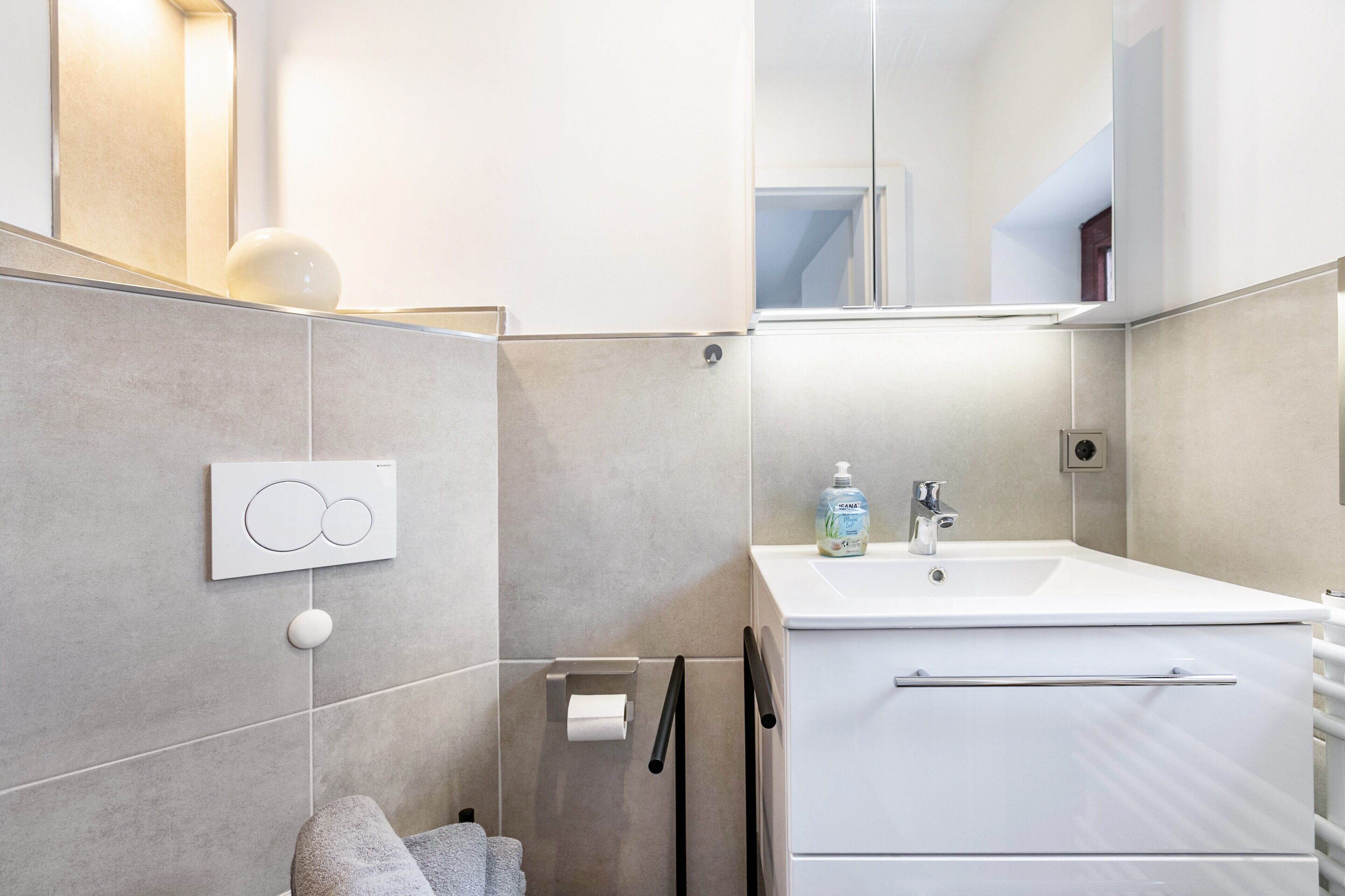 A modern bathroom with a white sink, a mirror, and a towel rack.
