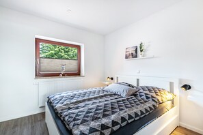 A bedroom with a bed, window, radiator, wall-mounted shelf, and bedside lamp. - Apartment '2' with Wi-Fi (Weddingstedt/OT Weddinghusen)