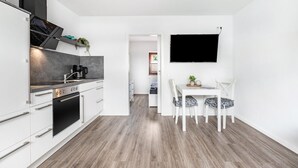 A modern kitchen with white cabinetry, a built-in oven, and a coffee maker. There is a dining area with a white table and chairs, and a flat-screen TV mounted on the wall. - Apartment '2' with Wi-Fi (Weddingstedt/OT Weddinghusen)