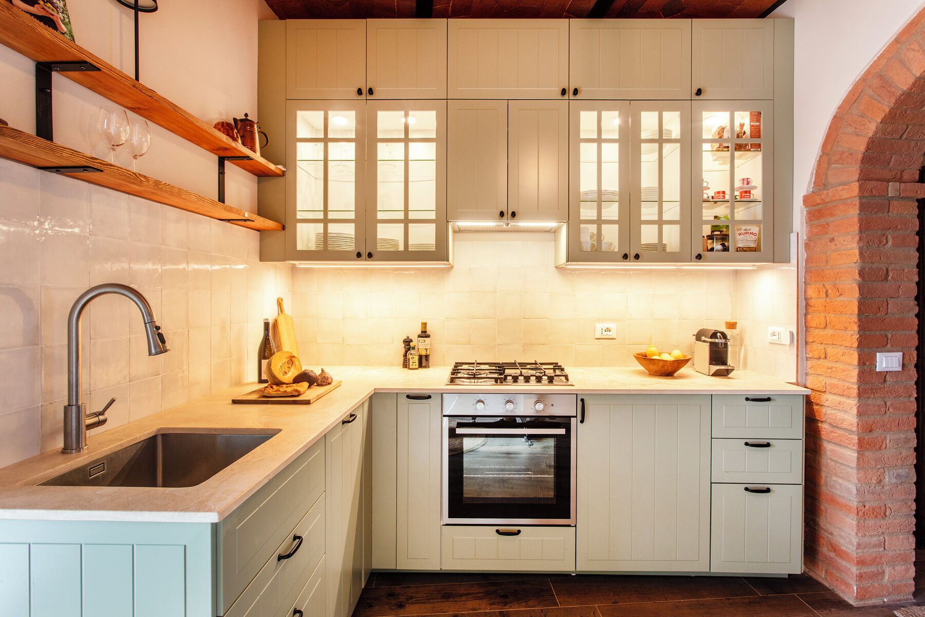 Una cucina compatta con mobili bianchi, forno integrato, lavello e ripiano in legno sopra il lavello.