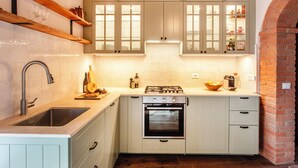 A compact kitchen with white cabinets, a built-in oven, a sink, and a wooden shelf above the sink. - Town house with garden in charming Tuscan hilltop village (San Pancrazio)