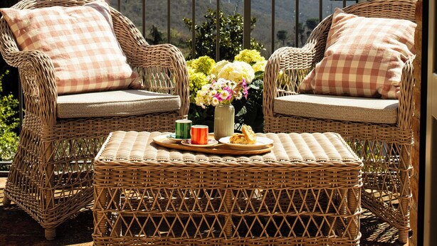 A wicker chair and table set on a balcony with a view of hills and a house in the background. - Town house with garden in charming Tuscan hilltop village (San Pancrazio)