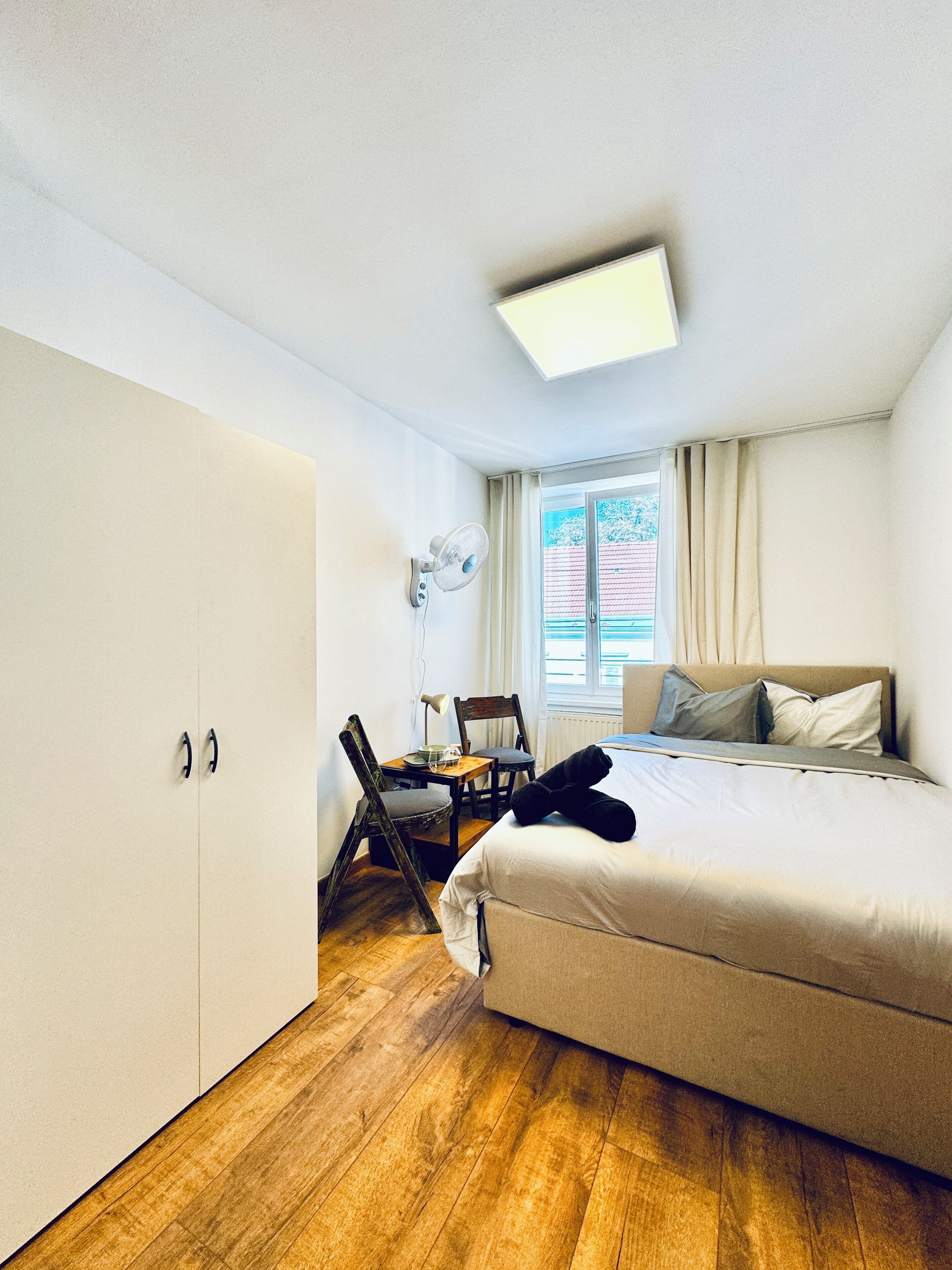 Une chambre à coucher avec un lit, un bureau et une chaise, une armoire et une fenêtre avec des rideaux.