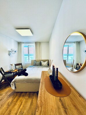 A hotel room with a bed, a desk, a chair, a mirror, and a window with curtains. - Cozy 5BR Apartment Near Kaufpark (Vienna)