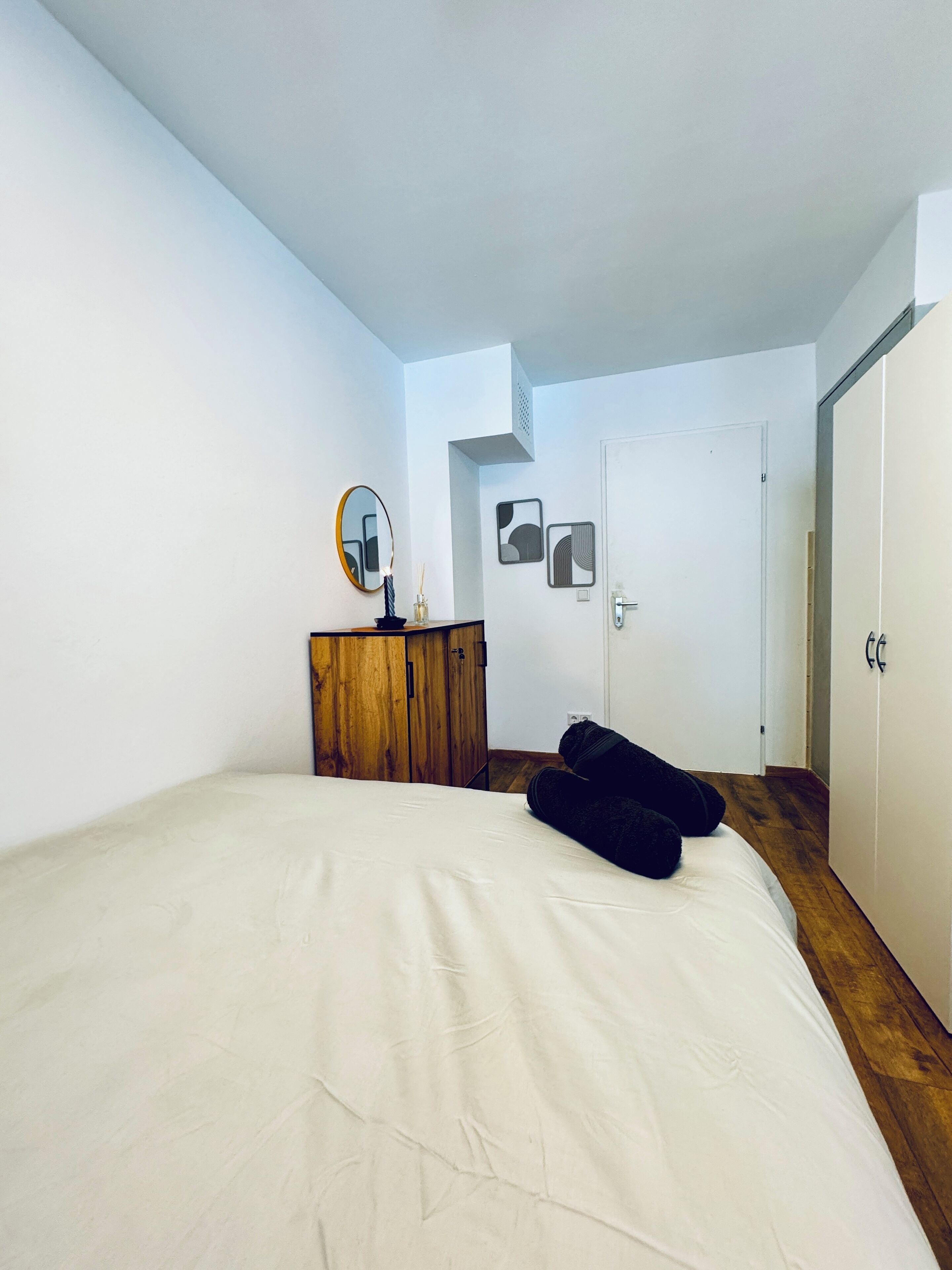 Een slaapkamer met een bed, een houten dressoir, een spiegel en een deur.