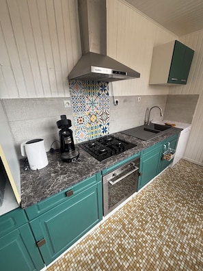 A kitchen with teal cabinets, a gas stove, a coffee maker, and a tiled backsplash.