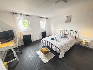 A bedroom with a bed, a desk, a chair, a radiator, and a TV.