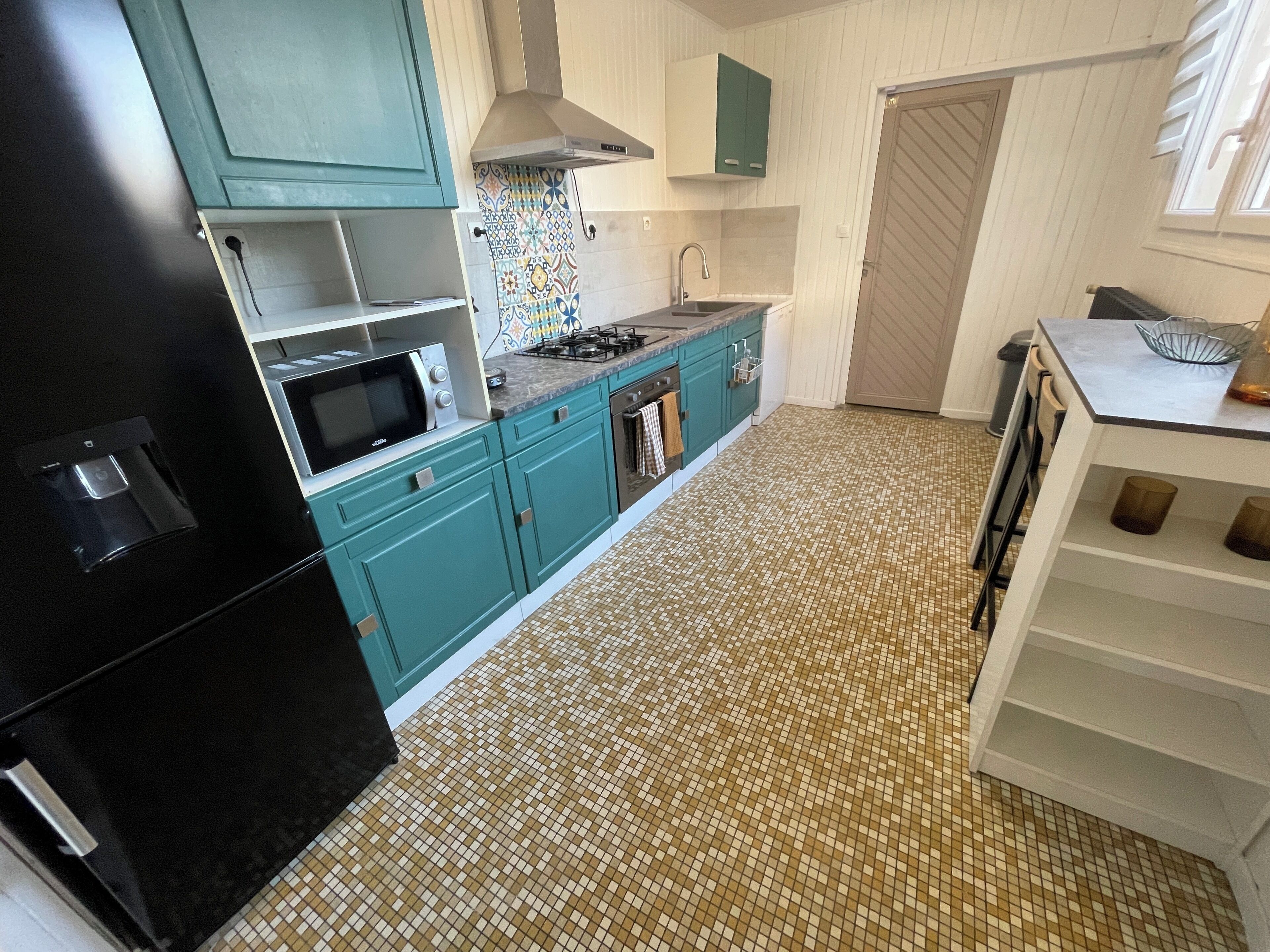 Une cuisine avec des armoires de couleur turquoise, un réfrigérateur noir, un four à micro-ondes, une cuisinière et un dosseret carrelé.