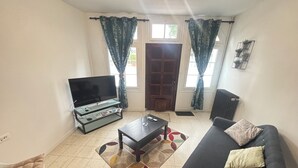 A living room with a sofa, a coffee table, a TV on a stand, and curtains. - Cosy 3-bedroom house - ideal for families and groups (Brionne)