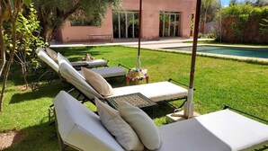 A poolside area with lounge chairs and a table, surrounded by a well-maintained lawn and a building in the background. - Villa Zeitouna (Ourika)
