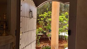 A doorway with a decorative metal grille, leading to an outdoor garden area with plants and a tiled floor. - Villa Zeitouna (Ourika)