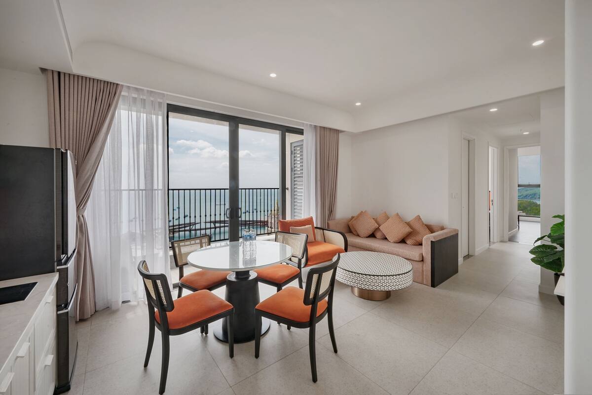 A modern living room with a round dining table, orange chairs, a sofa with cushions, and a TV.