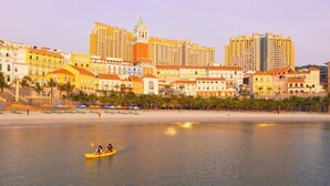 A coastal cityscape with a beach, a yellow kayak on the water, and a row of colorful buildings in the background. - CITY APARTMENT SUNSET TOWN (Phu Quoc)