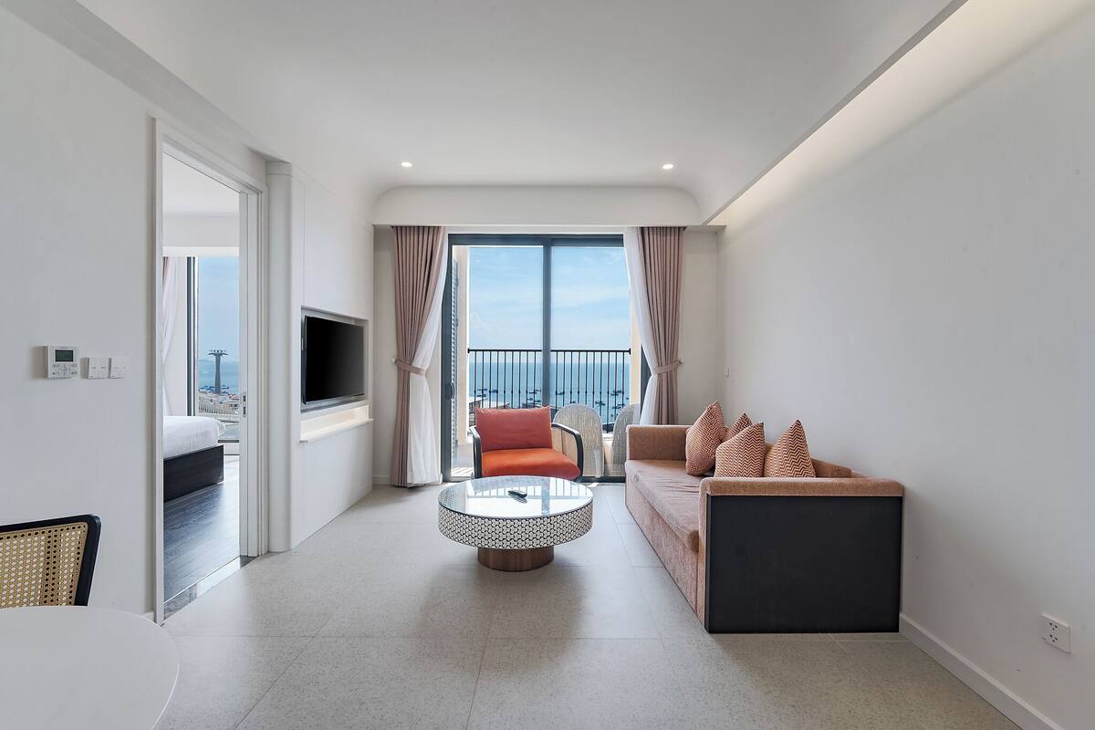 A modern hotel room with a balcony, a round coffee table, a sofa, and a TV.