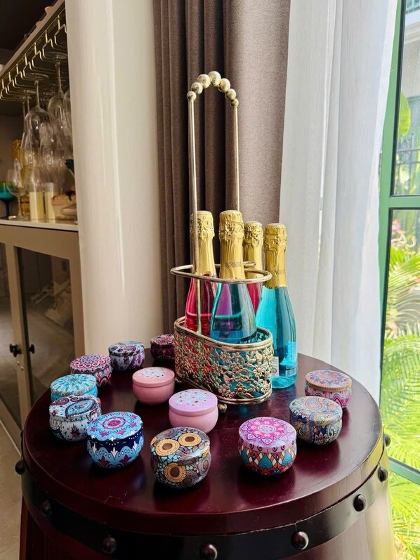 A round wooden table with a decorative metal stand holding three champagne bottles, surrounded by colorful, patterned containers. - CITY APARTMENT SUNSET TOWN (Phu Quoc)