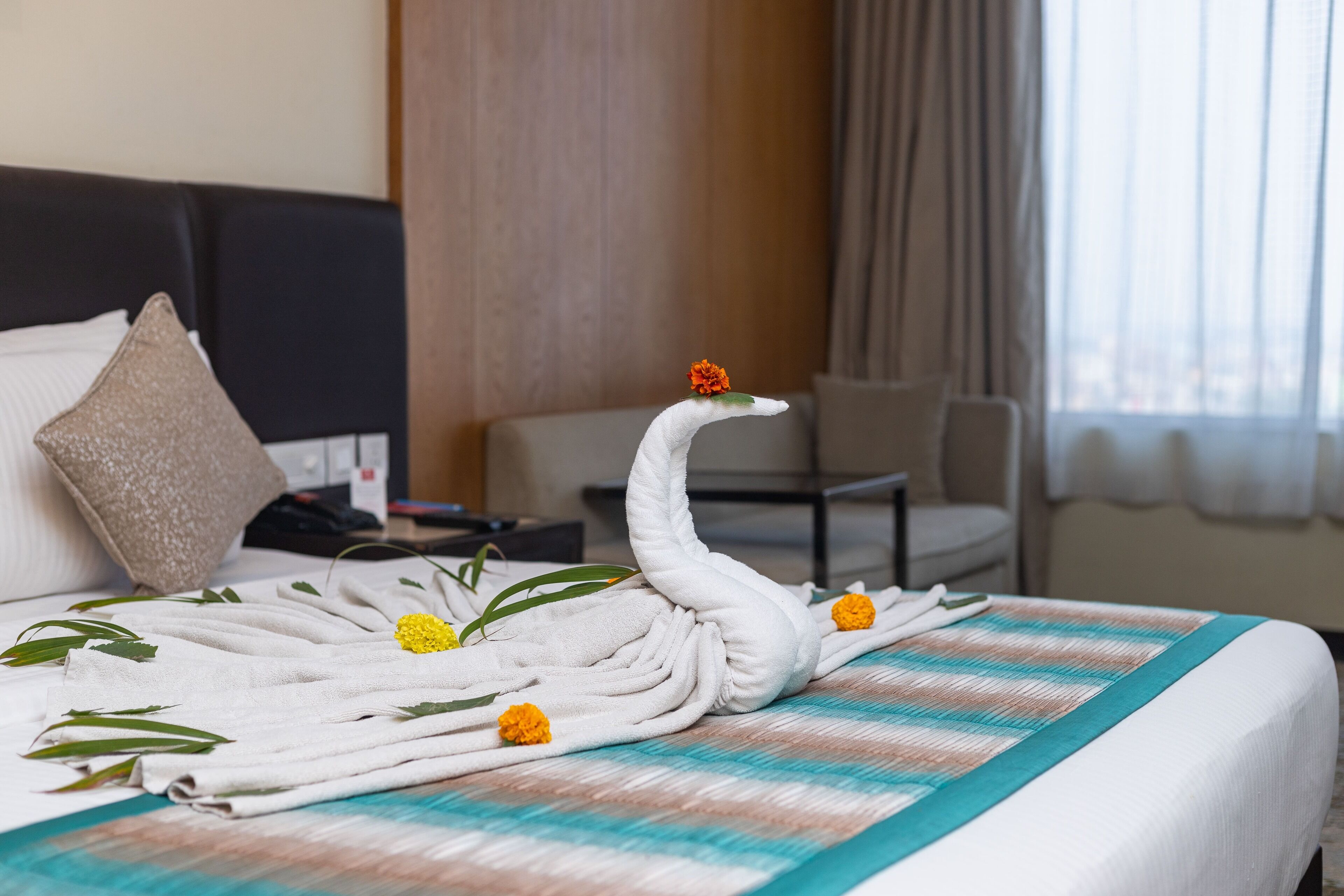 A neatly made bed with a swan towel headpiece, marigold flowers, and green leaves.
