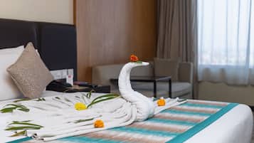 A neatly made bed with a swan towel headpiece, marigold flowers, and green leaves.
